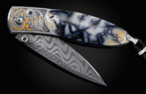 Handcrafted pocket knife from William Henry features a hand-engraved skull and intricate designs with 24K gold inlaid with fossil Woolly Mammoth tusk and set with spinel gemstones. The blade is damascus steel.
