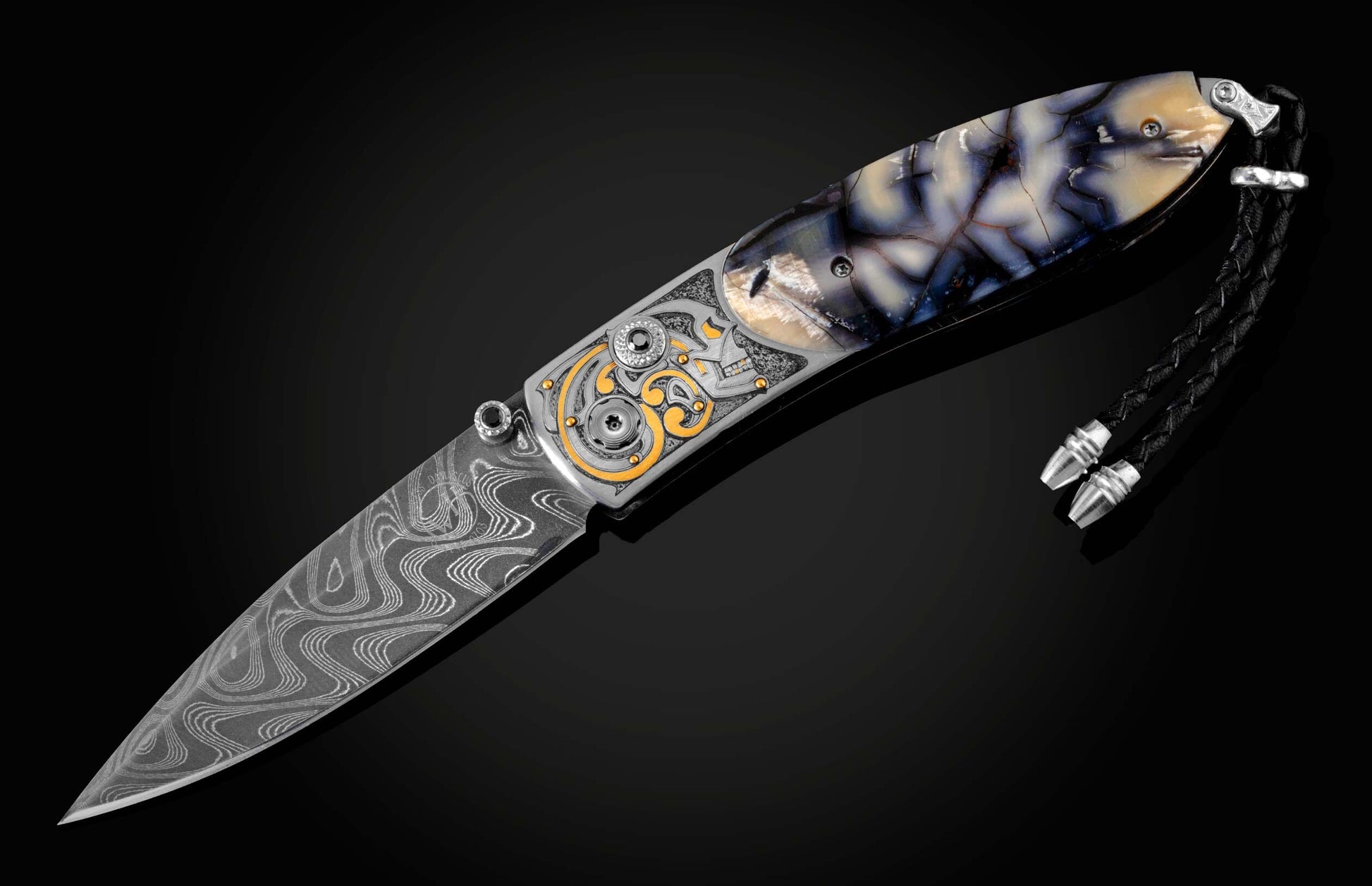 Handcrafted pocket knife from William Henry features a hand-engraved skull and intricate designs with 24K gold inlaid with fossil Woolly Mammoth tusk and set with spinel gemstones. The blade is damascus steel.