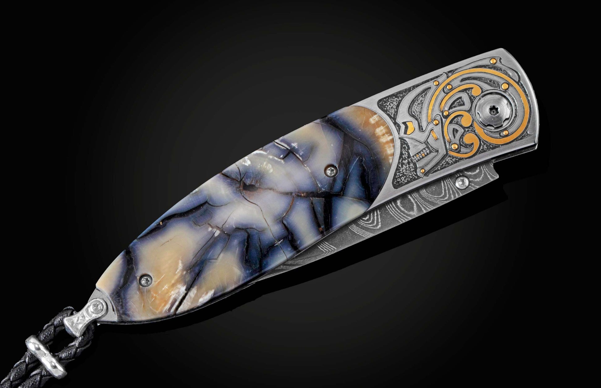 Handcrafted pocket knife from William Henry features a hand-engraved skull and intricate designs with 24K gold inlaid with fossil Woolly Mammoth tusk and set with spinel gemstones. The blade is damascus steel.