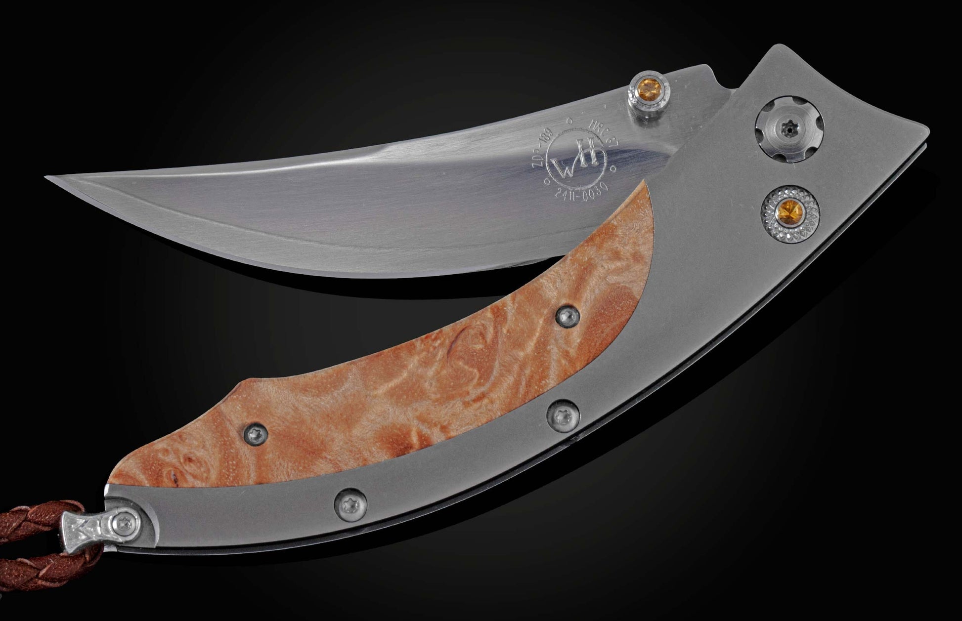 Handcrafted pocketknife from William Henry features a titanium frame inlaid with maple burl wood. The button lock and the thumb stud have been set with fine citrine gemstones. The knife is shown partially open on a black background.